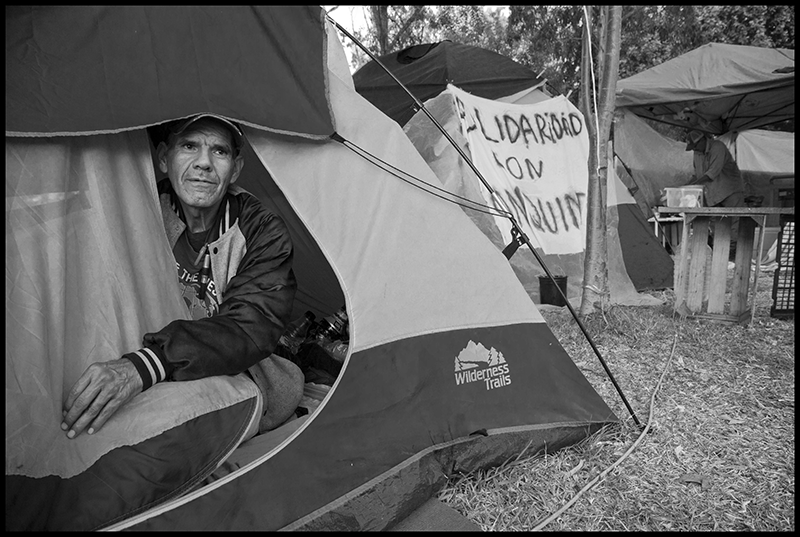 Daniel Taramayateca is a poet living in the encampment. Behind him is a banner saying 